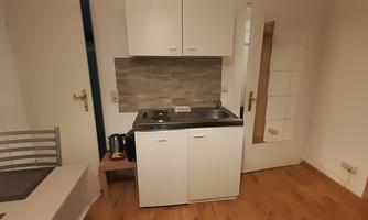 A small kitchen with white cabinets and a cooking hob. The floor is made of wood, and the space feels bright and cozy.
