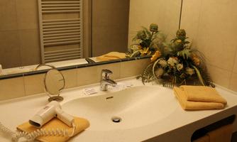 A modern bathroom with a sink, towels, and a hairdryer. Fresh flower arrangements are also on the shelf.