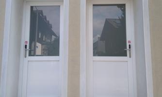 Two white doors with glass windows, mounted on a light wall. In the background, the silver reflection of buildings can be seen.