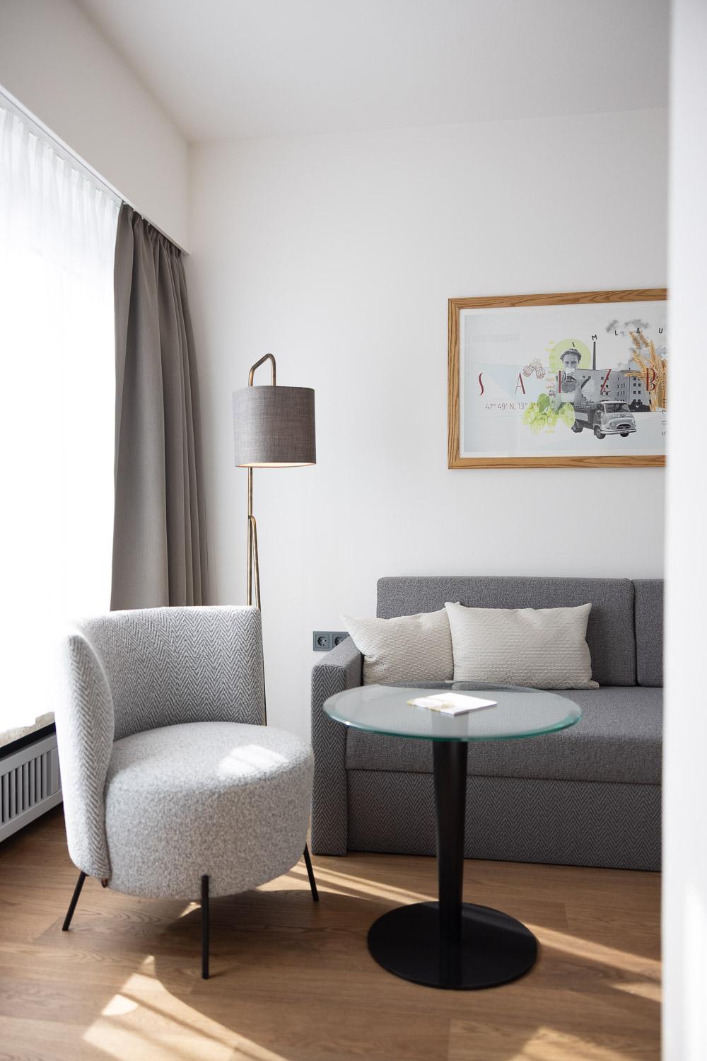A modern interior with a cozy armchair and a gray sofa. A round glass table and a floor lamp stylishly complete the room.