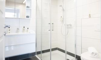 A modern bathroom with a glass shower and white tiles. On the shelf are toiletries and fresh towels.