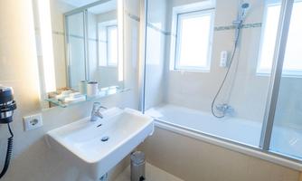 A modern bathroom with a sink and a shower. The large windows provide plenty of natural light.