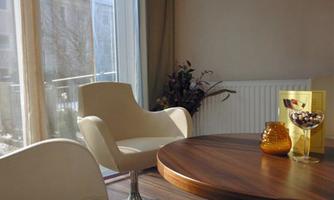 A modern room with a round wooden table and comfortable white chairs. Plenty of daylight enters through large windows, creating a relaxing atmosphere.