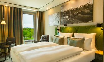 A modern hotel room with a double bed, comfortable pillows, and a cozy armchair. View through the window of a green landscape.