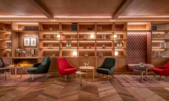 A stylishly furnished room with cozy armchairs in red and blue. In the background, there is an elegant bookshelf wall with lighting and decorative objects.