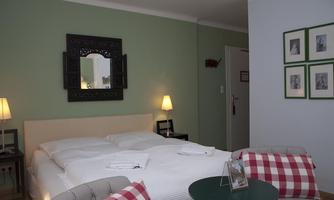 A cozy bedroom with a large bed and soft colors. Next to the bed are lamps and a small table with decorative elements.