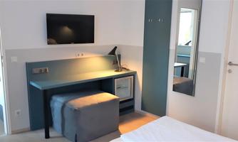 A modern room with a television on the wall, a desk, and a large mirror. The decor is designed in light colors and appears inviting.