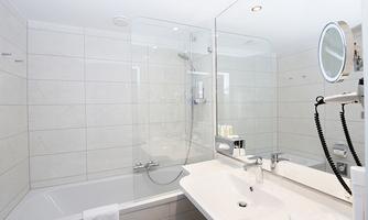 A modern bathroom with a bathtub and a separate shower. The walls are brightly tiled and there is a large mirror with lighting.