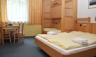 A simple bedroom with two beds and yellow sheets. A table with chairs and a window with curtains are also visible.