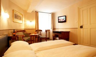 A cozy hotel room with two beds, a table, and chairs. The room is bright and cheerfully furnished, with a TV on the wall.