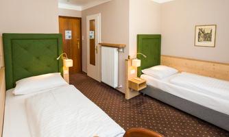 A spacious room with two single beds, a small nightstand, and a mood-setting wall mural. The walls are painted in neutral colors, creating a cozy atmosphere.