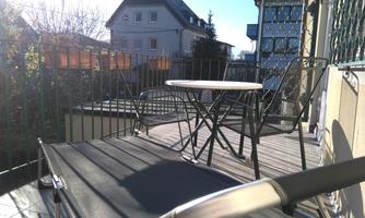 A cozy balcony with a small table and chairs. The sun is shining, and there is a view of the surroundings.