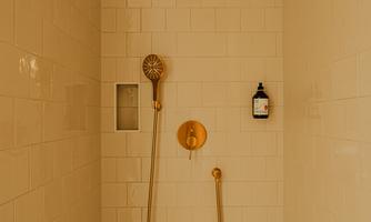 An elegant shower with golden fixtures and white tiles. The room feels modern and inviting.