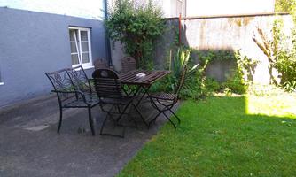 A cozy garden with a table and six chairs. Surrounded by grass and some plants.