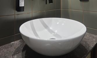 A modern sink made of white ceramic on a dark countertop. The walls are in soft green tones, with a minimalist faucet.