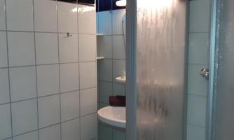 A simple bathroom with a shower cabin and a sink. The walls are covered with white tiles.