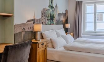 A modern bedroom with a cozy double bed and a stylish nightstand. In the background, a picturesque wall design is visible, showing a city view.