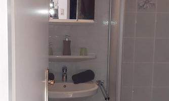 A modern bathroom with a shower and a sink. The walls are brightly tiled and the floor is dark.