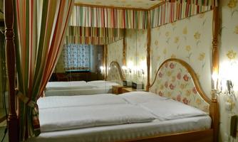 A cozy bedroom with two beds and a decorative canopy. The walls are designed with a floral pattern and colorful stripes.