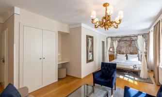A cozy room with an elegant chandelier and blue armchairs. The room features a large bed and plenty of daylight.