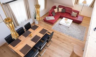 A modern living room with a red sofa and a large dining table. The room is brightly and warmly furnished, with wooden floors and elegant decorations.