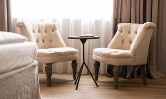 Two elegant beige armchairs are positioned by a small table. Soft light filters through the window, creating a cozy atmosphere.