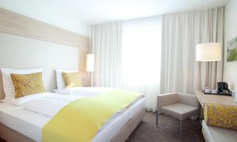 A modern hotel room with two single beds and light wood interior. The room is cheerful and well-lit, with cozy decor.