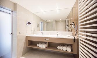 A modern bathroom with bright tiles and a large mirror. Fresh towels are neatly stacked on the wooden shelf.