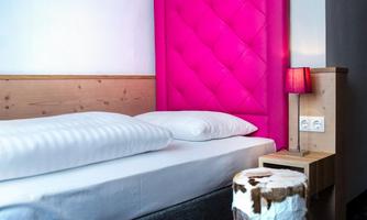 A modern bedroom with a striking pink headboard and a cozy bed. Next to the bed is a nightstand with a lamp and an interesting stool.