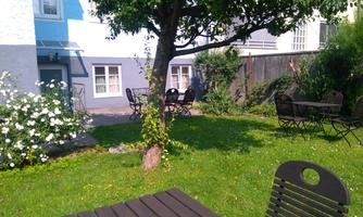 A quiet garden with green grass and blooming shrubs. There are several tables and chairs for relaxing outdoors.