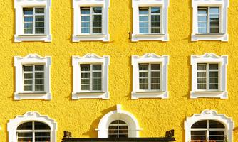 A yellow building with white window frames. Flower boxes hang above the entrance.