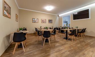 A modern restaurant with wooden floors and black chairs. Pictures hang on the walls, and there is a large window front.