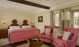A cozy bedroom with a large bed and two comfortable armchairs. The decor has a warm and inviting atmosphere.