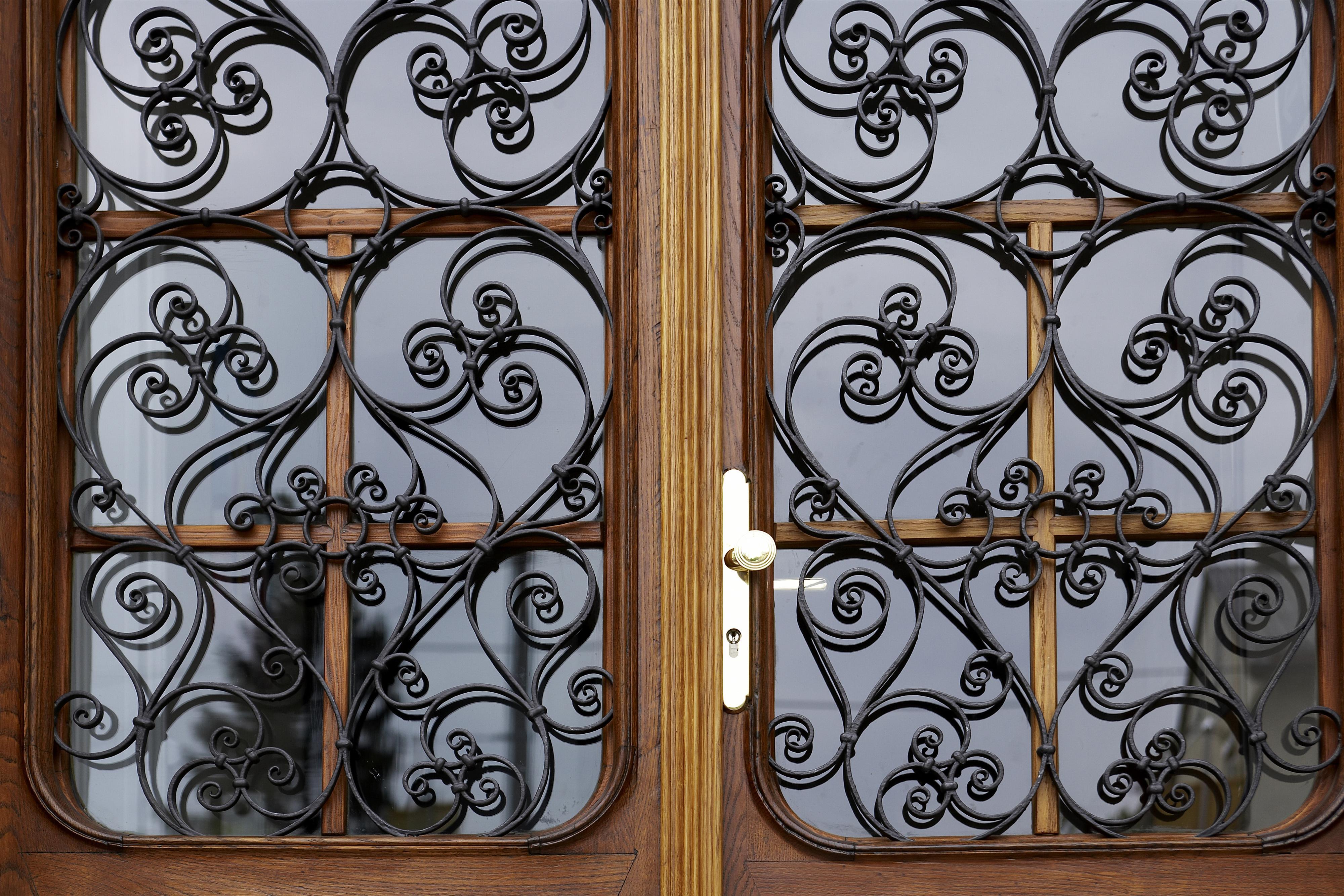 Two wooden doors with elaborate, curved iron slats. The embellishments create an elegant and stylish appearance.