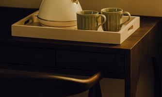 A teapot stands on a tray next to two cups. The table has a simple, elegant wooden surface.