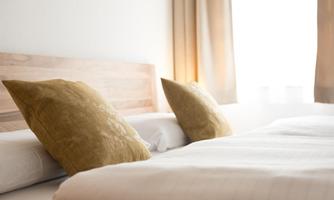 A cozy bedroom with two pillows on a bed. The light softly falls through a window with curtains.