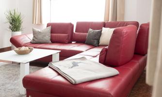 A modern living room with a red leather sofa and several cushions. A white coffee table is in the middle and a plant is in the corner.