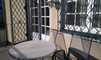 A sunny balcony with a round table and chairs. The windows in the background are adorned with an elegant lattice.