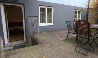 A cozy courtyard with an entrance to a room. There is a table with chairs and gray walls in the background.
