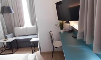 A modern room with a cozy sofa and a desk. A television and a small plant complete the decor.