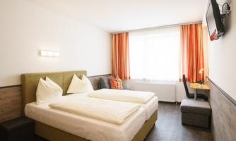 A modern hotel room with a large bed and elegant furnishings.  
Bright curtains provide plenty of daylight and a cozy atmosphere.
