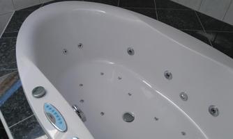 A modern whirlpool with multiple jets. The tub is white and is situated on a dark tiled floor.