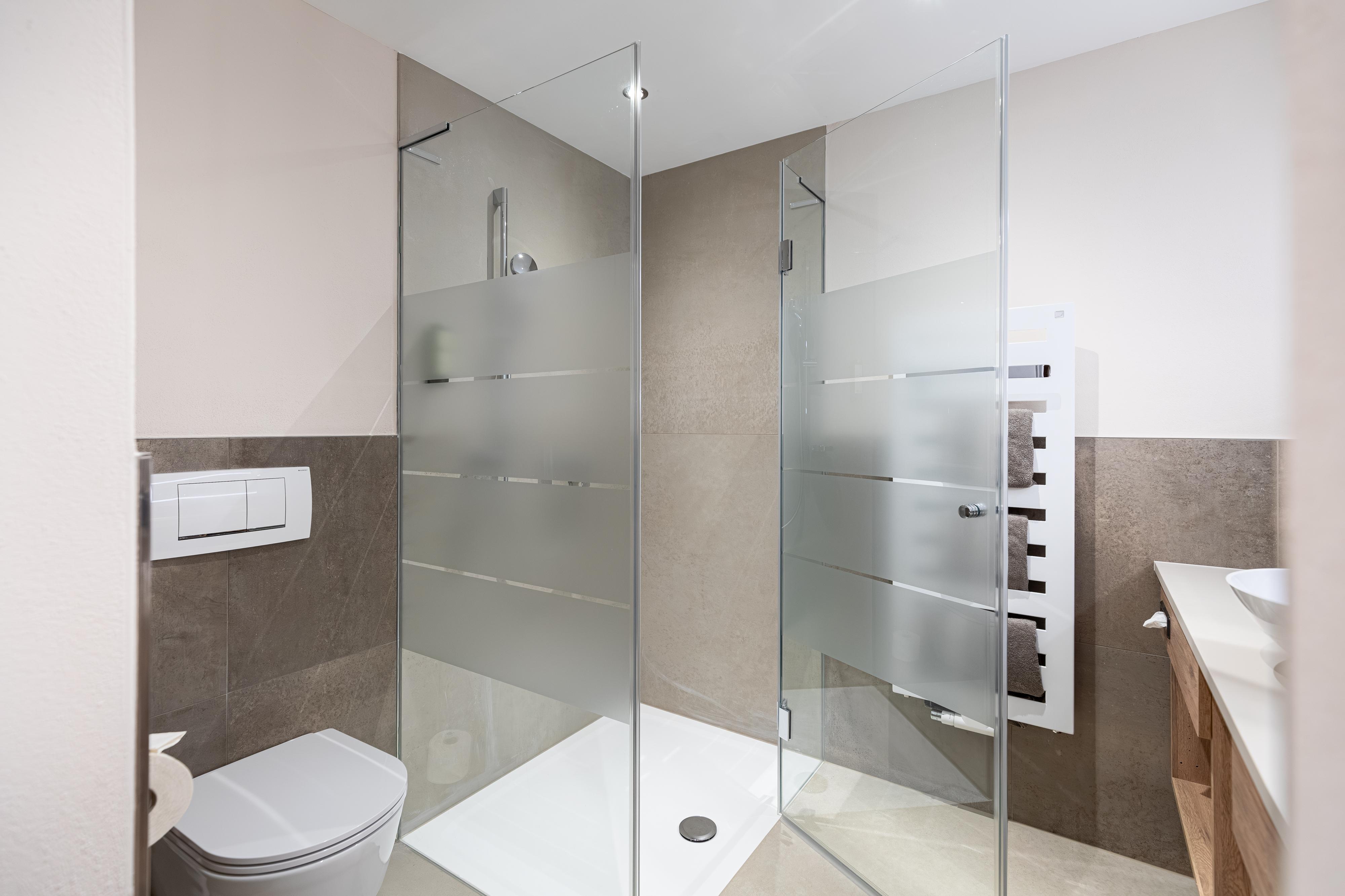 A modern bathroom with a glass shower and an elegant toilet. The walls are in neutral colors and the furnishings are stylish.