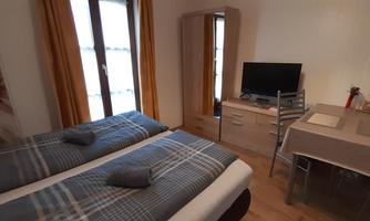 A cozy bedroom with two single beds and a desk. The room is bright and decorated in a modern style, with a green view through the windows.