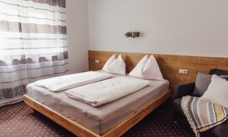A cozy bedroom with a double bed and wooden details. Soft light streams into the room through the window.