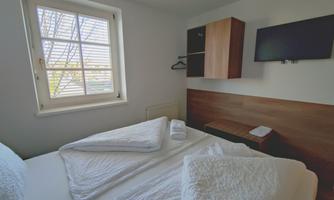 A cozy room with a double bed and a television on the wall. The window lets in natural light and creates a bright atmosphere.