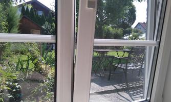 A view of a garden with a table and chairs outside. In the background, a few trees and a building are visible.