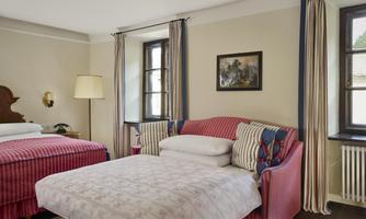 A cozy room with red and blue furnishings. There are two beds and a sofa as well as large windows that let in natural light.