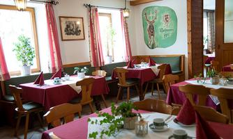 A cozy restaurant with red-covered tables and windows that let in plenty of daylight. On the wall, there is a simple, rustic mural.
