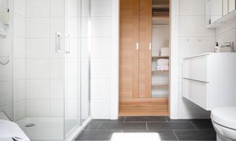 A modern bathroom with a shower and a large mirror. The floor is fitted with dark tiles and there is a wooden cabinet in the background.